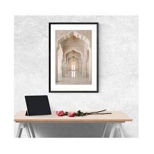 May include: A framed photograph of a white hallway with arched doorways and a chandelier hanging from the ceiling. The hallway is lined with white columns and the floor is tiled.