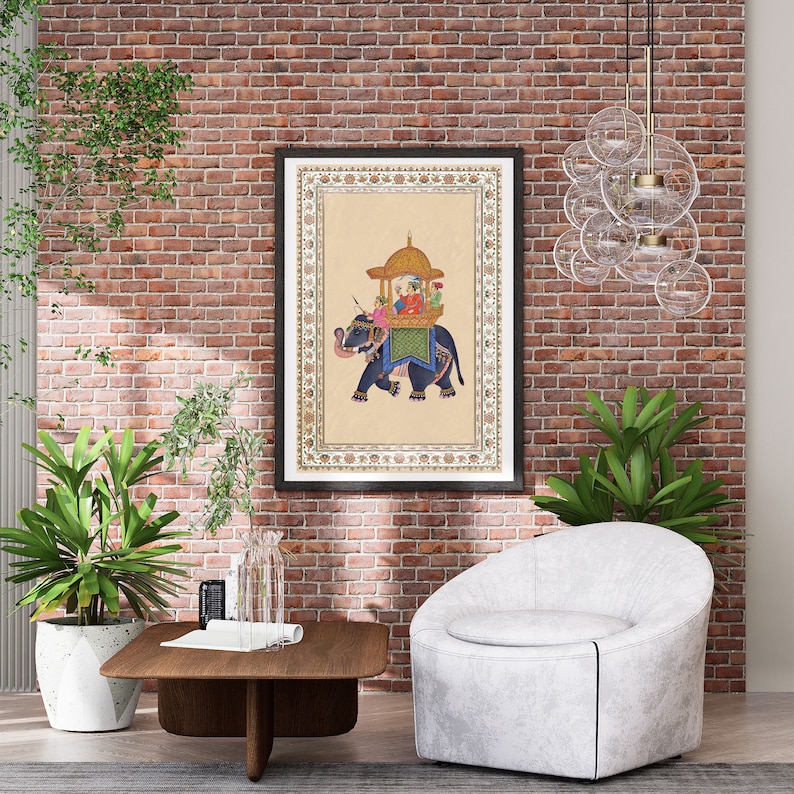 以下が含まれることがあります： 伝統的なインドの絵画が描かれた額装されたプリント。絵画は、華やかな衣装を着た王族が象に乗っている様子を描いています。象はカラフルな装飾で飾られています。絵画はベージュの背景に描かれ、黒い額縁で囲まれています。