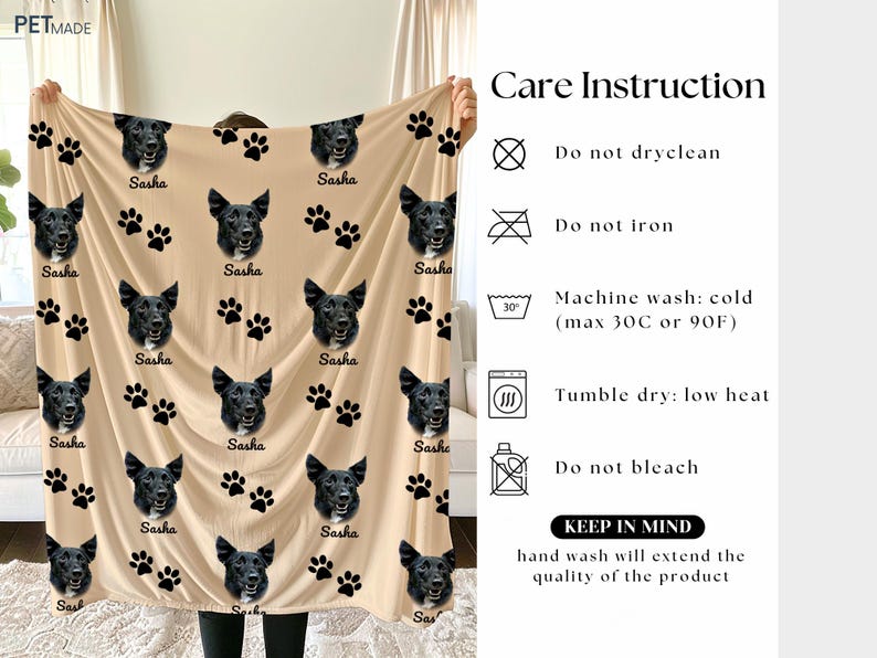 a person holding up a beige blanket with black paw prints and the word "Sasha" printed on it. The blanket has a care instruction label attached to it, providing guidelines for washing and care.