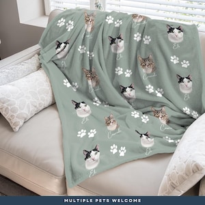 A cozy gray blanket with cat faces and paw prints is draped over a white couch, creating a warm and inviting atmosphere.