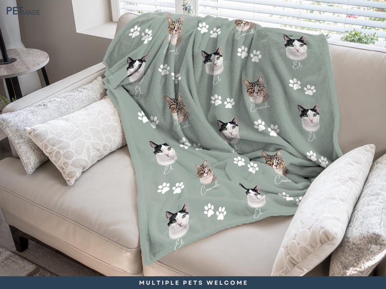 A cozy gray blanket with cat faces and paw prints is draped over a white couch, creating a warm and inviting atmosphere.