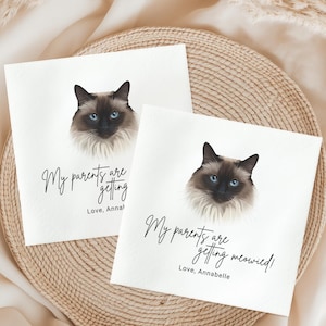 two white cards with a cat's face on them, placed on a woven basket. The cards have text that reads "My parents are getting married!" and "Love, Annabelle".