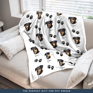 A white couch with a blanket featuring a dog's face and paw prints on it.