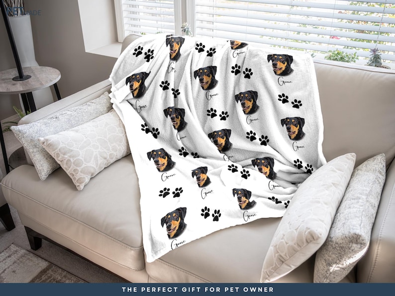 A white couch with a blanket featuring a dog's face and paw prints on it.