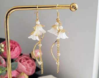 Op de afbeelding: Een paar gouden oorhangers met witte bloemencharms en heldere kralen die aan een delicate ketting hangen.