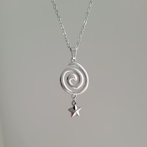 May include: A silver necklace with a spiral pendant and a small star charm. The chain and pendant are made of a shiny metal, creating a minimalist and elegant design. The star charm hangs below the spiral.