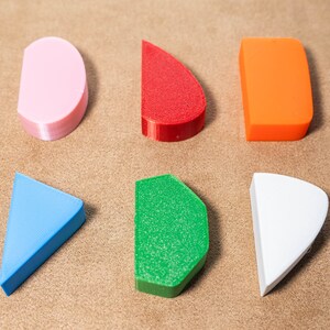 May include: Six geometric shapes made of different colours. The shapes are a pink half-circle, a red half-circle, an orange rectangle, a blue triangle, a green half-circle, and a white half-circle.