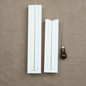 May include: Two white plastic beading tools with rows of holes, and a small wooden awl with a metal tip.