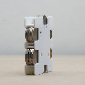 May include: White plastic coin holder with slots for different coin denominations. The holder has numbers 1, 2, 5, 10, 25, 50, and 100 printed on it.