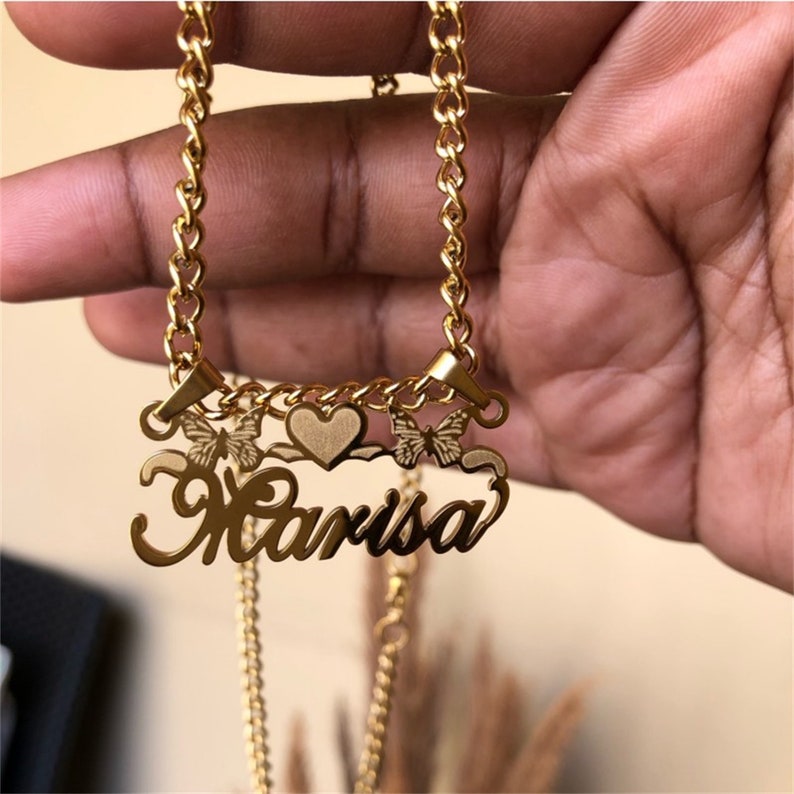 K&ouml;nnte beinhalten: Goldkette mit einem Namensschild in Kursivschrift, auf dem "Marisa" steht, mit zwei Schmetterlingsanh&auml;ngern und einem Herzanh&auml;nger.