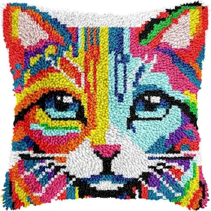 May include: A square throw pillow cover featuring a latch hook or tufted design of a cat face. The cat is rendered in a vibrant, multi-colored palette including bright yellow, orange, pink, light blue, and purple, with large dark blue eyes.