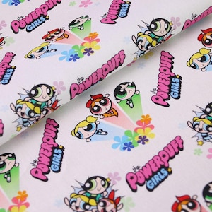 Puede incluir: Tela blanca con un patrón repetido de los personajes de dibujos animados de las Supernenas. El diseño incluye las palabras "The Powerpuff Girls" en rosa, junto con imágenes de Pétalo, Burbuja y Cactus.