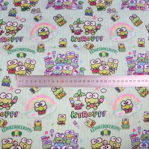 May include: Green fabric with a repeating pattern of a cartoon frog character named Keroppi. The fabric has a light green background with white stripes and features a rainbow, palm trees, and other cartoon elements. The text "Keroppi" and "Kerokerokeroppi" appears on the fabric.