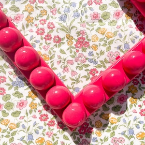 May include: A pink heart-shaped frame with a raised, textured surface. The frame is made of plastic and has a glossy finish.