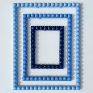 May include: Three blue frames made of plastic with a textured surface. The frames are nested inside each other, creating a layered effect. The innermost frame is the darkest blue, followed by a lighter blue, and the outermost frame is the lightest blue.