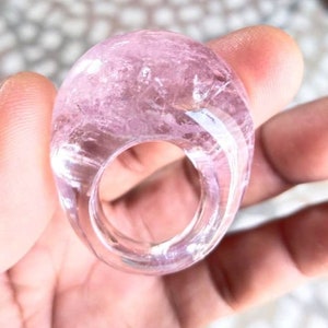 Op de afbeelding: Een roze kristallen ring met een glad, afgerond ontwerp. De ring is gemaakt van één stuk kristal en heeft een brede, open band.