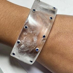 May include: A clear quartz bangle bracelet with small blue gemstones set around the edge.