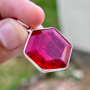 Könnte beinhalten: Ein sechseckiger Anhänger mit einem tief roten Edelstein, der in Silber gefasst ist.