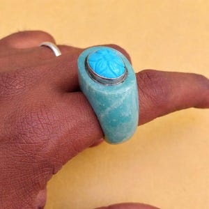 以下が含まれることがあります： シルバーのベゼルにセットされた、彫刻された花の模様が特徴のターコイズリング。 リングは、お揃いのターコイズ色の幅広バンドを備えた、分厚いスタイルです。 リングは指に表示されています。