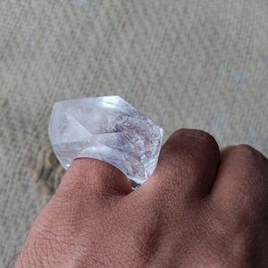 May include: A clear quartz crystal ring, worn on a finger.