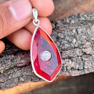 Może przedstawiać: Wisiorek w kształcie łzy z czerwonego kamienia szlachetnego z srebrną zawieszką i mniejszym opalem w środku.