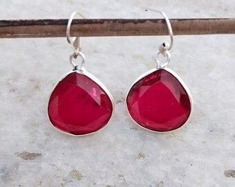 Peut inclure: Une paire de boucles d'oreilles pendantes argentées. Chaque boucle d'oreille présente une pierre précieuse rouge foncé, taillée en forme de goutte d'eau, sertie dans un sertissage argenté. Les boucles d'oreilles sont suspendues à de simples crochets argentés.