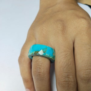 May include: A turquoise ring with a white inlay. The ring is made of natural stone and has a unique, organic shape.