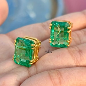May include: A pair of emerald green gemstone earrings with gold settings. The earrings are rectangular in shape and have a polished finish.