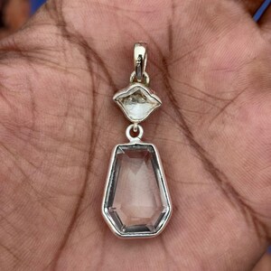 Pu&ograve; includere: Un pendente in argento con due pietre preziose chiare e sfaccettate. La pietra superiore &egrave; a forma di diamante, mentre quella inferiore &egrave; un esagono allungato pi&ugrave; grande. Il pendente &egrave; sospeso da un'ansa in argento.