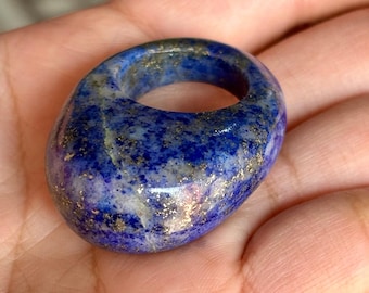 Puede incluir: Un anillo grande de forma ovalada hecho de lapislázuli azul con motas doradas. El anillo es liso y pulido.