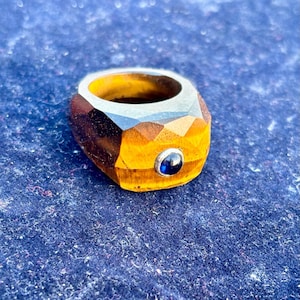 May include: A gold and brown ring with a faceted design and a blue gemstone in the center.
