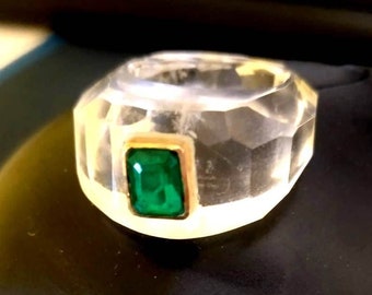 Puede incluir: Un anillo transparente facetado con una piedra preciosa verde engastada en un engaste de oro.