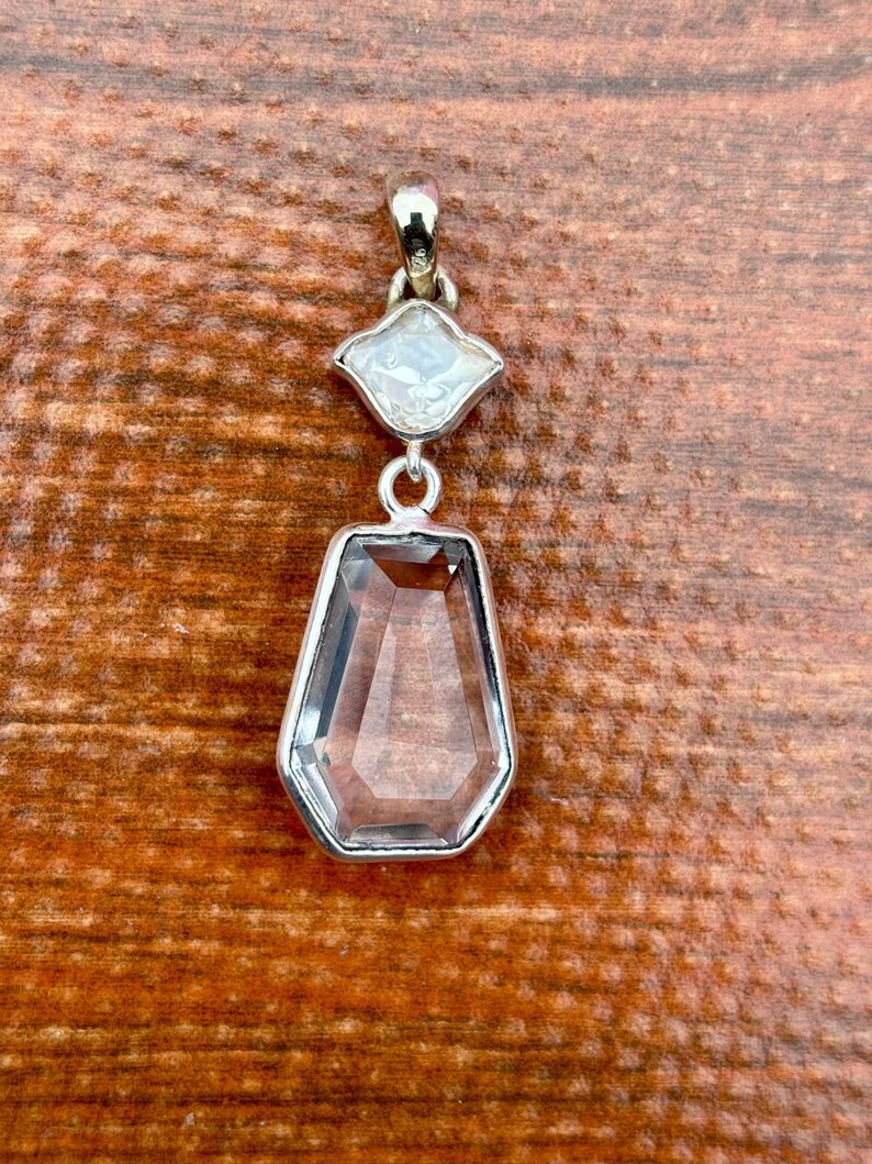 Pu&ograve; includere: Un pendente in argento con due pietre preziose trasparenti. La pietra superiore &egrave; una gemma bianca a forma di diamante, e quella inferiore &egrave; una gemma rettangolare, trasparente e sfaccettata. Il pendente &egrave; appeso a una cauzione d'argento.