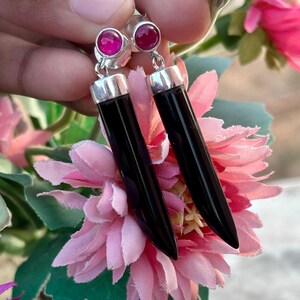 May include: A pair of dangle earrings with black onyx teardrop-shaped stones and pink gemstone accents.