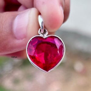 Puede incluir: Un colgante de plata en forma de corazón con una gran piedra preciosa roja brillante.