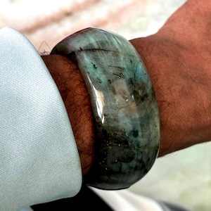 May include: A green and gray gemstone bangle bracelet. The bracelet is made of a smooth, polished stone with a unique pattern.