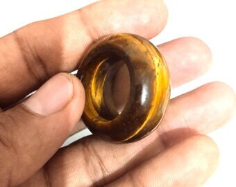Puede incluir: Un anillo de piedra de ojo de tigre marrón y dorado. El anillo está hecho de una piedra lisa y pulida y tiene una forma ovalada redondeada.