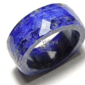 May include: A wide blue lapis lazuli ring with gold flecks. The ring is faceted and has a polished finish.