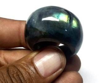 Puede incluir: Un anillo de piedra preciosa azul oscuro y verde con destellos iridiscentes. El anillo está hecho de una piedra lisa y pulida y tiene una forma redondeada.