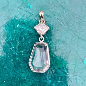 Pu&ograve; includere: Un pendente in argento con due pietre preziose chiare e sfaccettate. La pietra superiore &egrave; una piccola gemma a forma di diamante, mentre quella inferiore &egrave; una gemma pi&ugrave; grande a forma di goccia. Il pendente &egrave; appeso a una cauzione d'argento.