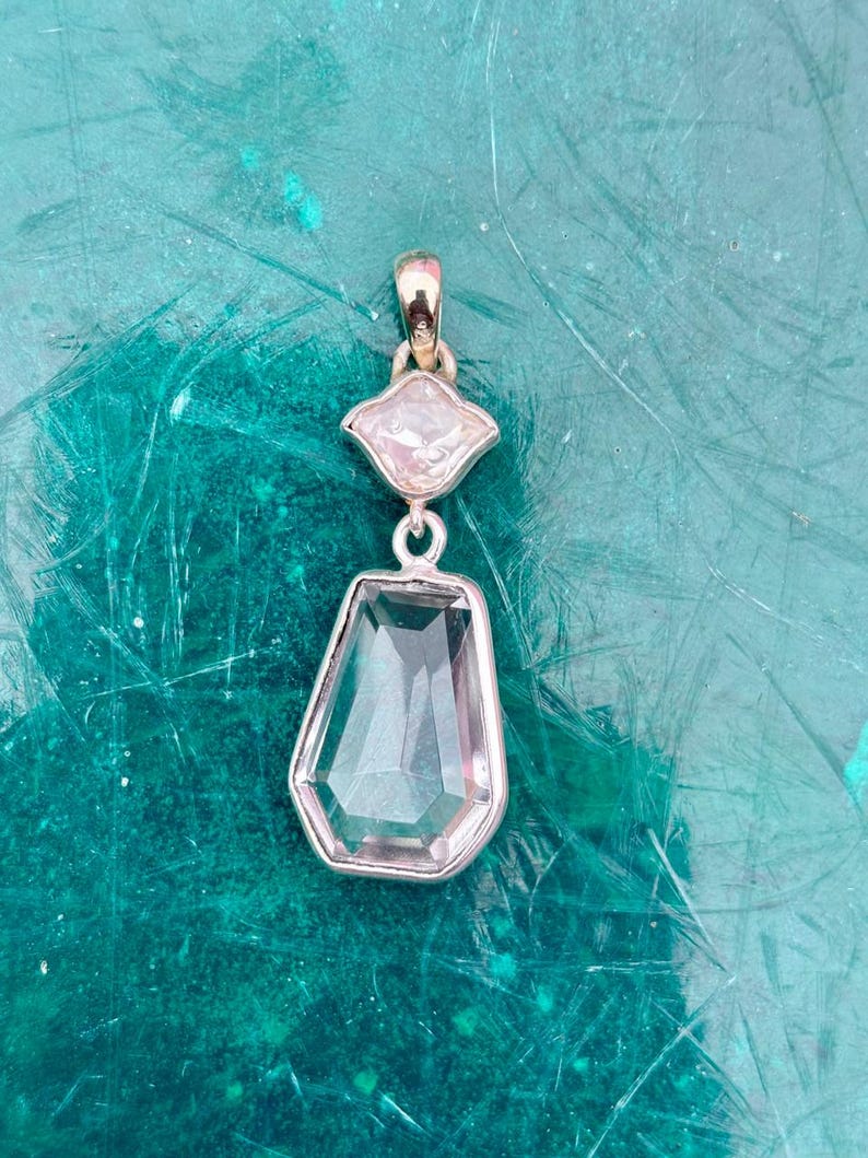 Pu&ograve; includere: Un pendente in argento con due pietre preziose chiare e sfaccettate. La pietra superiore &egrave; una piccola gemma a forma di diamante, mentre quella inferiore &egrave; una gemma pi&ugrave; grande a forma di goccia. Il pendente &egrave; appeso a una cauzione d'argento.
