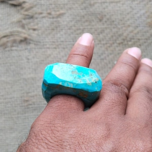 May include: A large, turquoise ring with a rough, irregular shape. The ring is made of natural turquoise stone and has a unique, organic look.