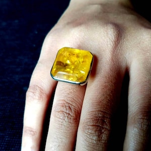 May include: A square-shaped amber ring with a silver setting. The amber is a bright yellow colour and has a translucent appearance.