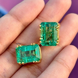 May include: A pair of emerald green gemstone earrings with gold settings. The earrings are rectangular in shape and have a faceted cut.