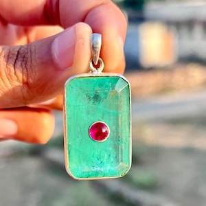 May include: A silver pendant with a rectangular green emerald gemstone and a small red ruby gemstone in the center.