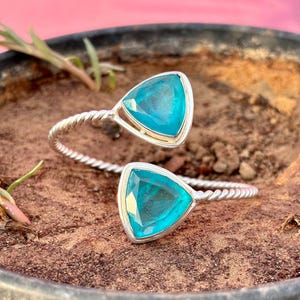 Può includere: Un braccialetto d'argento con due pietre triangolari turchesi. Il braccialetto ha un design intrecciato.
