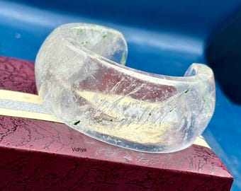 May include: A clear, translucent bangle bracelet with a subtle green hue and a rough, textured surface. The bracelet is made of resin and has a unique, organic look.