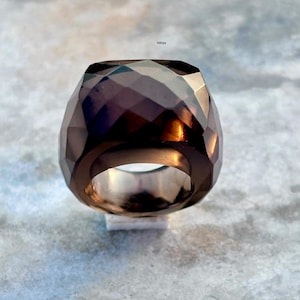 May include: A faceted, dark brown ring with a geometric design. The ring has a wide band and a large, multi-faceted stone. The ring is set on a white surface against a light gray background. The word "Vidhya" is in the top right corner.