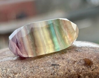 Puede incluir: Una gema de fluorita multicolor con un patrón estriado. La gema es de color púrpura claro, verde y amarillo. La gema está sentada sobre una roca.