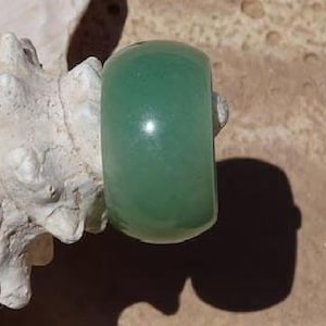 May include: A smooth, wide band ring crafted from a solid piece of translucent, light green stone. The ring features a polished, rounded exterior surface with a consistent, uniform color throughout the material, showing subtle natural variations.